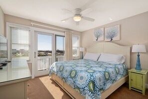 Ein Schlafzimmer mit einem Bett, einem Deckenventilator, einem Nachttisch mit Lampe und Blick durch eine Schiebetür.