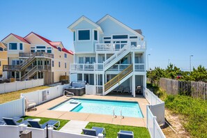 A two-story house with a pool, outdoor seating, and a staircase leading to a balcony.