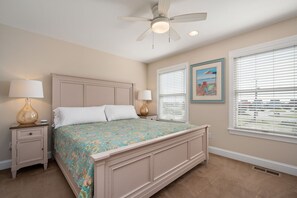 A bedroom with a bed, two bedside tables with lamps, a ceiling fan, and a window with blinds.