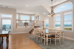 A spacious room with a dining table, chairs, and a view of the ocean through large windows.