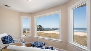 A room with a view of a beach and pier, featuring a large window, a chair, and a small table.