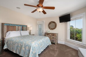 Une chambre à coucher comprenant un lit, un ventilateur de plafond, une commode, un miroir, un téléviseur et une fenêtre donnant sur un beau paysage.