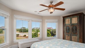 A bedroom with a large bed, a ceiling fan, and a view of the outdoors through large windows. - Hotel California: Semi-oceanfront, ocean views, private pool, hot tub, theater room, elevator. (Southern Shores)