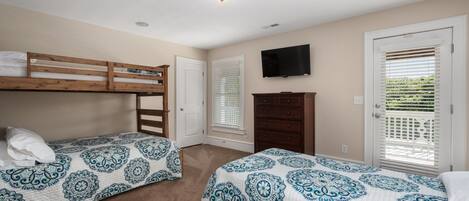 Un dormitorio con dos camas individuales, un aparador, un televisor y una puerta con persianas.