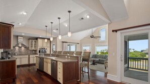 A spacious kitchen with a central island, wooden flooring, and pendant lighting. - Hotel California: Semi-oceanfront, ocean views, private pool, hot tub, theater room, elevator. (Southern Shores)