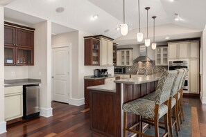 A modern kitchen with wooden cabinets, a central island, and bar stools. - Hotel California: Semi-oceanfront, ocean views, private pool, hot tub, theater room, elevator. (Southern Shores)