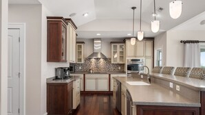 A modern kitchen with wooden cabinets, a tiled backsplash, and pendant lighting. - Hotel California: Semi-oceanfront, ocean views, private pool, hot tub, theater room, elevator. (Southern Shores)