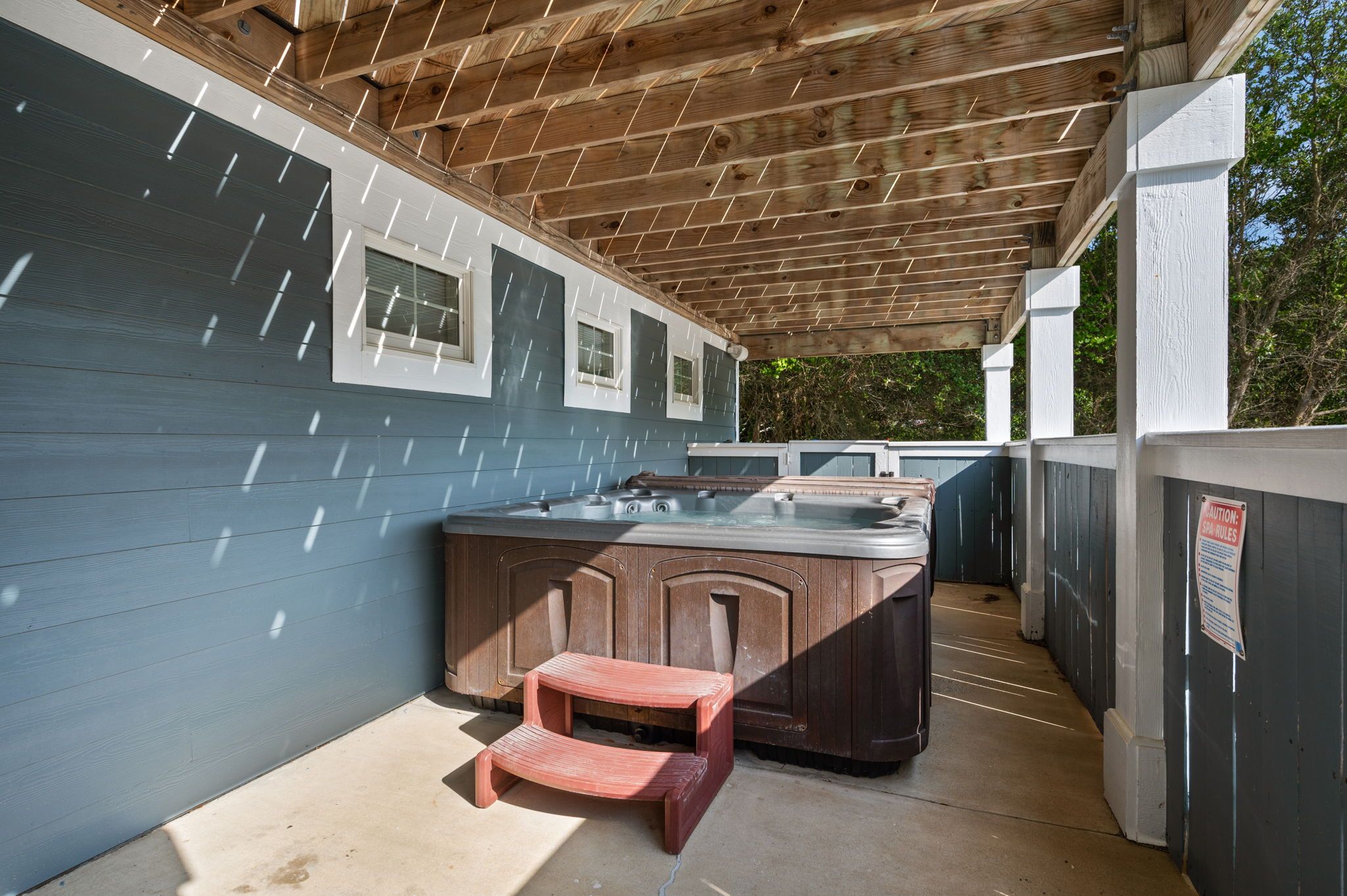 A covered outdoor area with a hot tub, a wooden bench, and a wooden pergola.