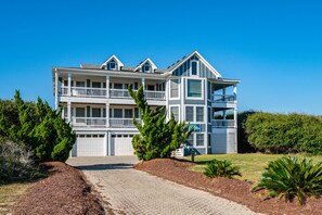 A multi-story residential building with a driveway, surrounded by greenery and a clear sky. - Hotel California: Semi-oceanfront, ocean views, private pool, hot tub, theater room, elevator. (Southern Shores)
