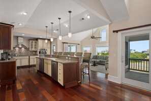 A spacious kitchen with a central island, wooden cabinets, and a dining area with a view. - Hotel California: Semi-oceanfront, ocean views, private pool, hot tub, theater room, elevator. (Southern Shores)