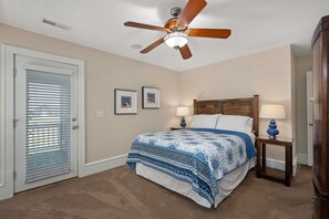 A bedroom with a bed, two bedside tables, a ceiling fan, and a door with blinds.