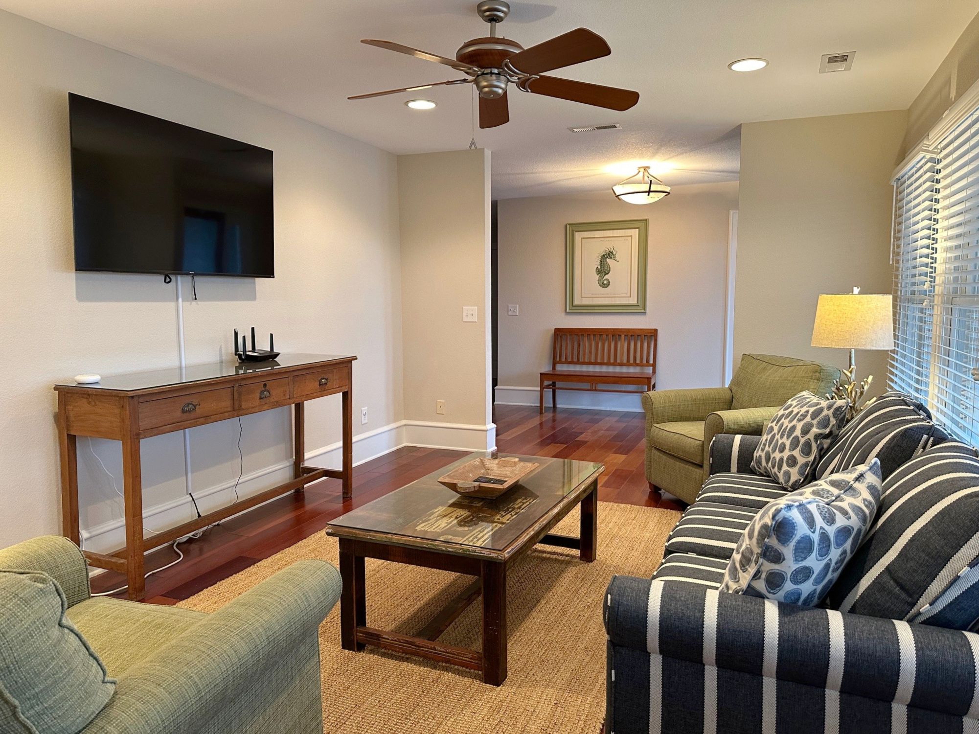 A living room with a flat-screen TV, wooden furniture, a ceiling fan, and a framed picture on the wall.