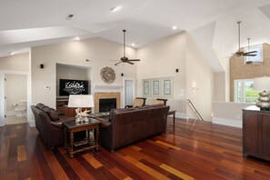 Un salon spacieux avec un grand canapé en cuir marron, une table basse en bois et un téléviseur à écran plat fixé au mur.