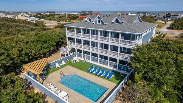 A multi-story building with a swimming pool, outdoor seating, and a view of the ocean. - Hotel California: Semi-oceanfront, ocean views, private pool, hot tub, theater room, elevator. (Southern Shores)