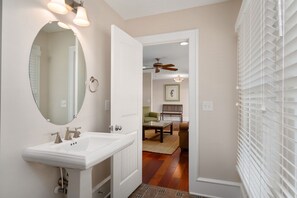 Une salle de bain avec un lavabo blanc, un miroir rond et un ventilateur de plafond.