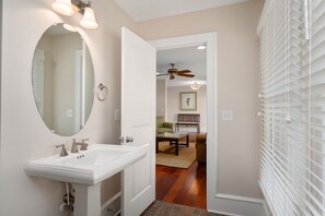 Une salle de bain avec un lavabo blanc, un miroir rond et un ventilateur de plafond.