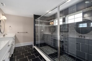 Une salle de bain moderne avec une douche à l’italienne en verre, un meuble-lavabo blanc doté d’un grand miroir et un sol carrelé en noir et blanc.
