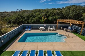 Une piscine rectangulaire agrémentée d’une pergola en bois et de chaises longues.