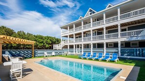 A pool area with a clear blue pool, lounge chairs, and a covered seating area. - Hotel California: Semi-oceanfront, ocean views, private pool, hot tub, theater room, elevator. (Southern Shores)