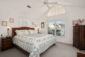 A bedroom with a wooden bed, a nightstand, a dresser, and a window with blinds.