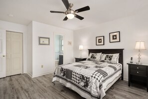 Une chambre à coucher comprenant un lit, un ventilateur de plafond, deux tables de chevet, une commode et une porte.