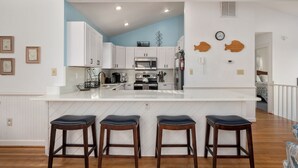 Een moderne keuken met witte kasten, een centraal eiland met krukken, en een blauwe accentmuur.