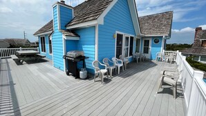 Een blauw huis met een terras, een barbecue en zitplaatsen buiten.