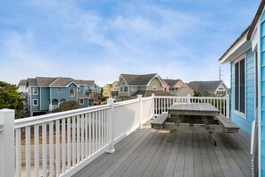 A wooden deck with a white railing, a picnic table, and a view of colorful houses in the background.