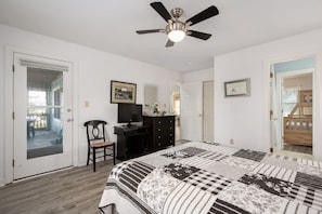 A bedroom with a bed, a ceiling fan, a television, a dresser, and a door leading to a balcony.