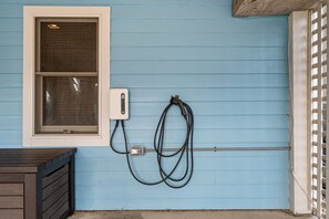 A blue exterior wall with a window, a power outlet, and a hose.