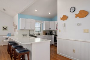 A kitchen with white cabinets, a central island with stools, a coffee maker, and decorative fish wall art.