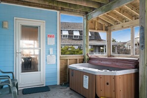 A hot tub area with a wooden deck, a door with a glass panel, and a view of houses in the background.
