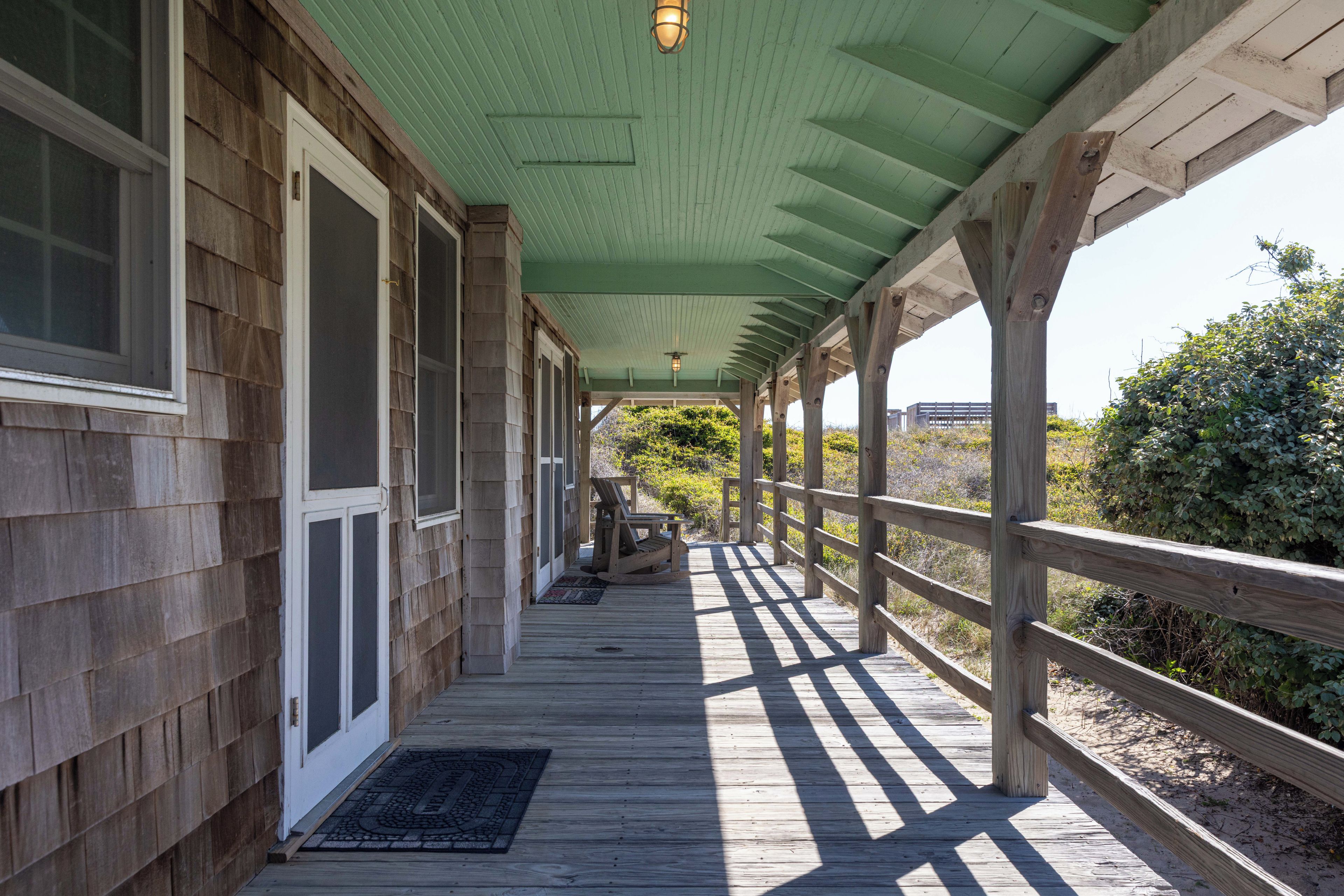 A covered wooden deck with a railing, a bench, and a door with a window.