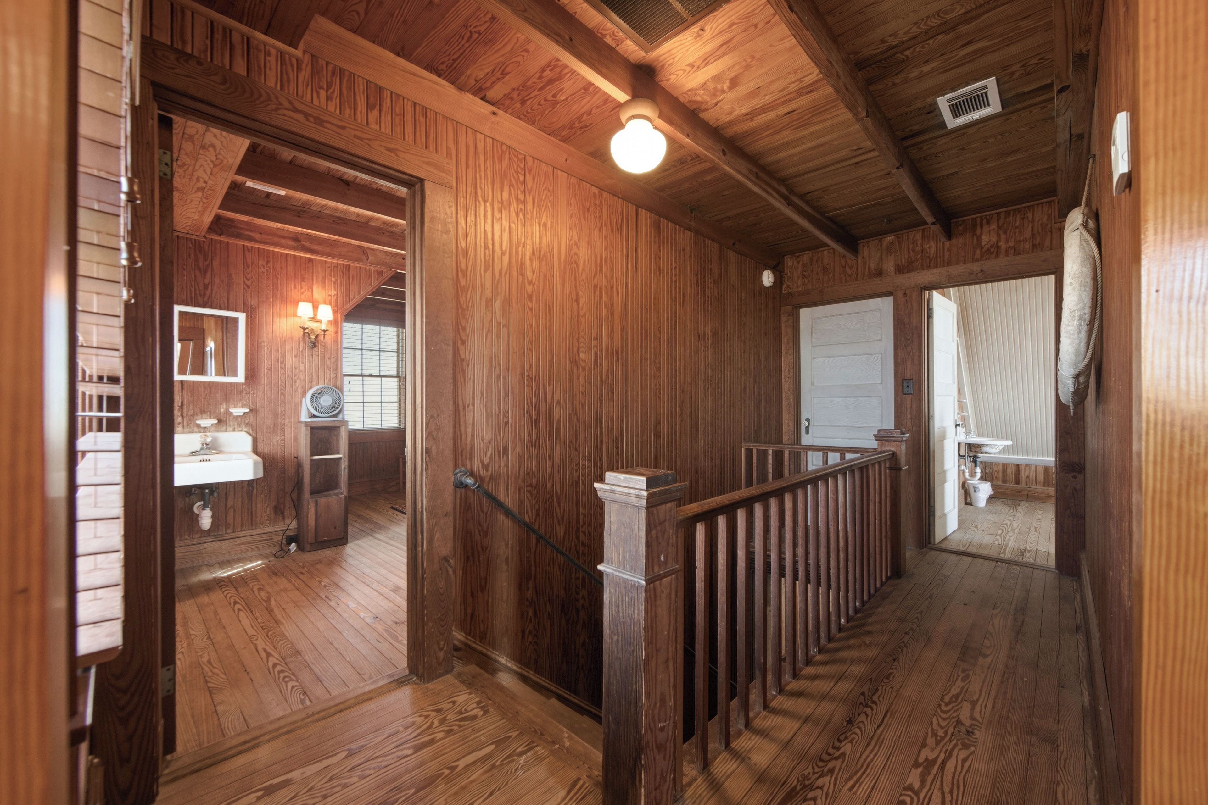 A wooden interior with a staircase, a white sink, and a fan.