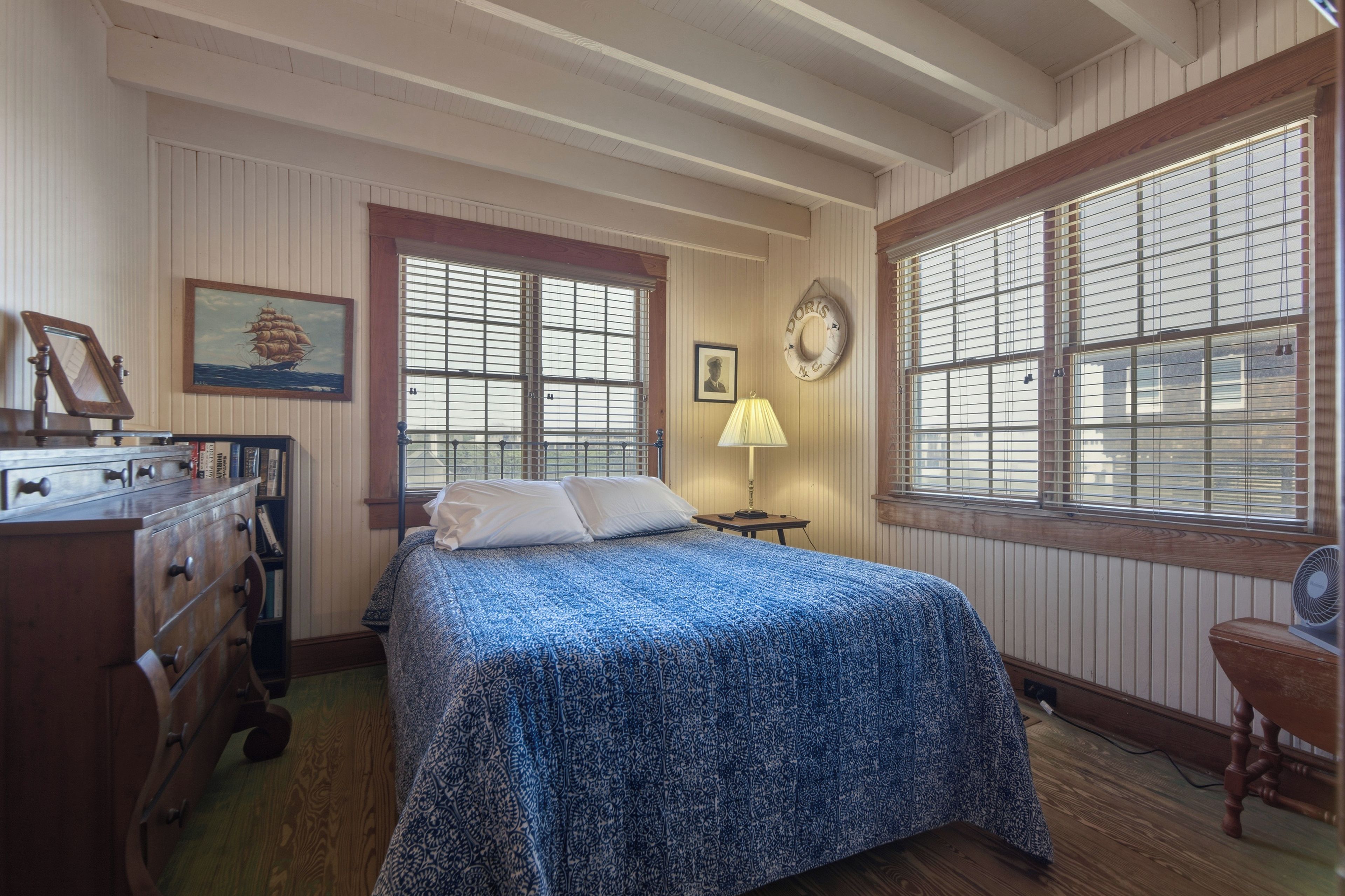 A room with a bed, dresser, lamp, and a window with blinds.