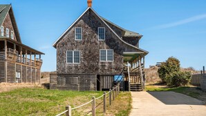A rustic wooden building with a gabled roof, a covered porch, and a small staircase leading to a door. - Nags Head 225:Historic oceanfront, sandy path to the beach, comfy & cozy (Nags Head)