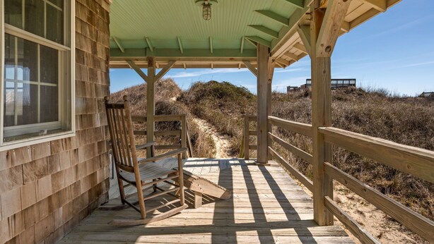 A wooden deck with a covered area, a bench, and a view of a sandy path leading to a hill. - Nags Head 225:Historic oceanfront, sandy path to the beach, comfy & cozy (Nags Head)