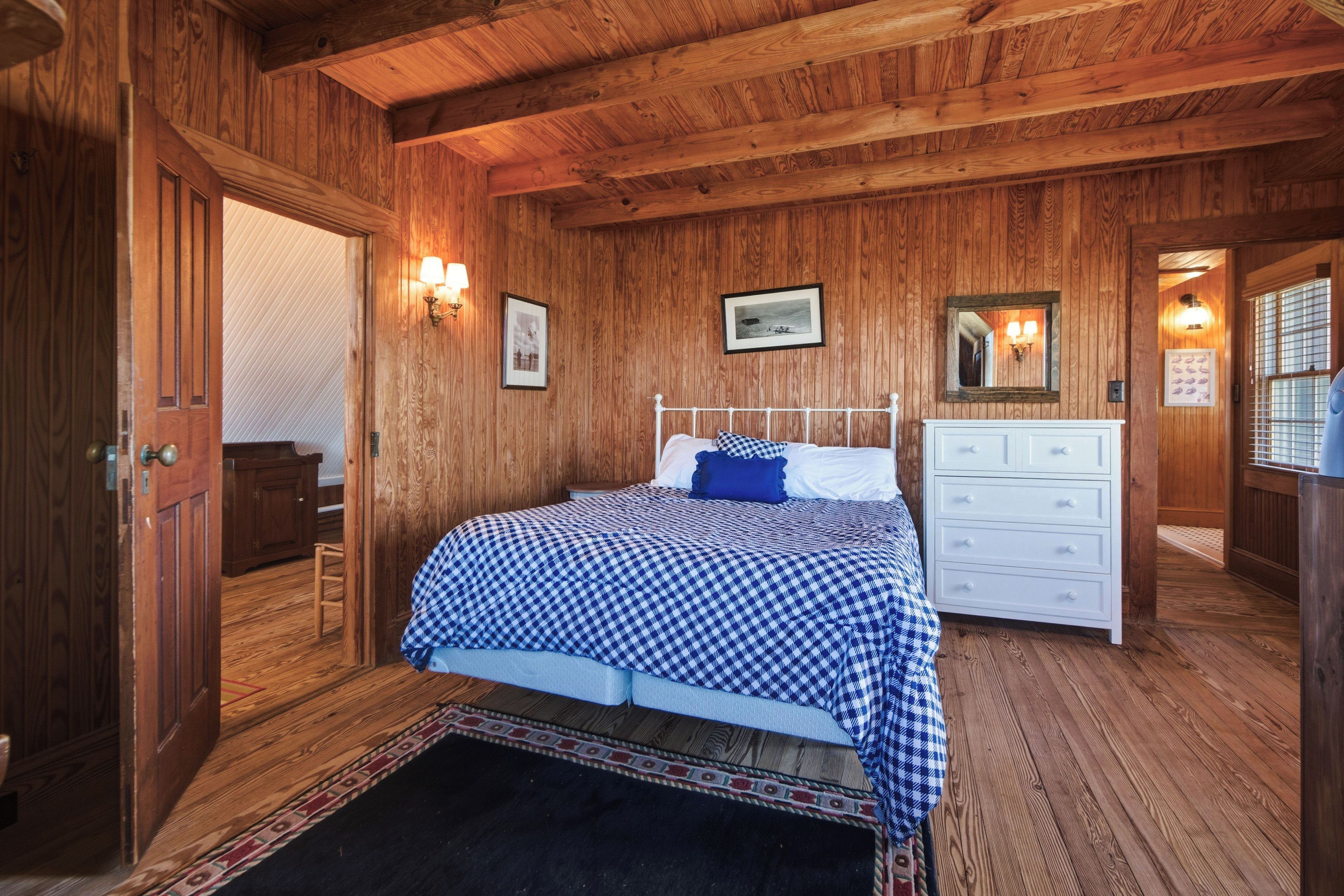 Une chambre aux murs lambrés, avec un lit, une commode et des lampes fixées au mur.