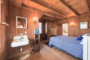 A wooden-paneled room with a bed, a sink, and a fan.
