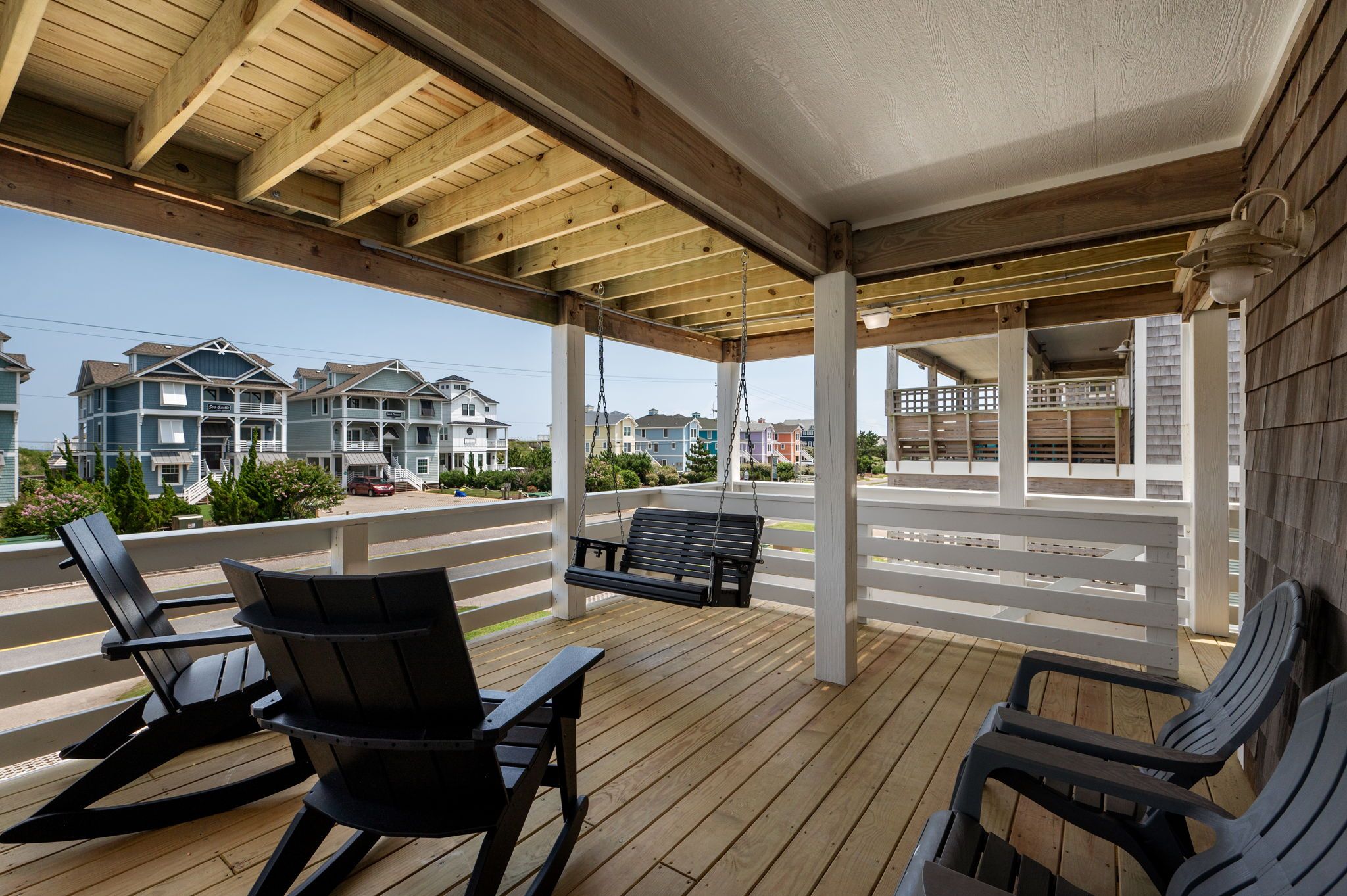 A covered outdoor seating area with wooden flooring and black chairs.