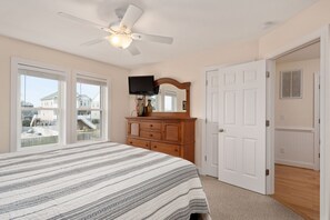 Une chambre à coucher avec un grand lit, un ventilateur de plafond, une commode, un téléviseur et une porte donnant sur une autre pièce.