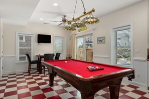 Une table de billard recouverte d’un feutre rouge, entourée de chaises, dans une pièce dont le sol est décoré d’un motif à carreaux.