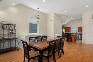 A spacious dining area with a wooden table and chairs, a bookshelf, and a window with a view.