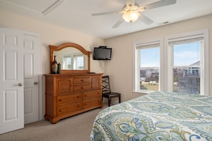 A bedroom with a bed, dresser, television, and a view of the neighborhood.
