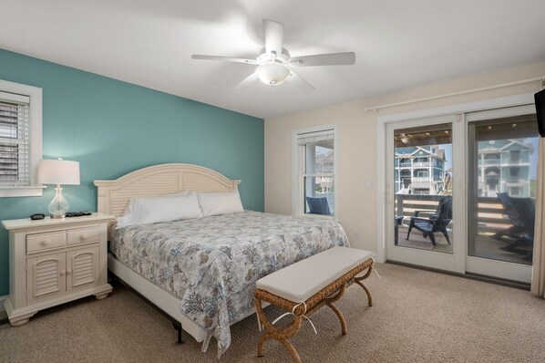 A bedroom with a bed, bedside table, lamp, and a view of a balcony with outdoor furniture.