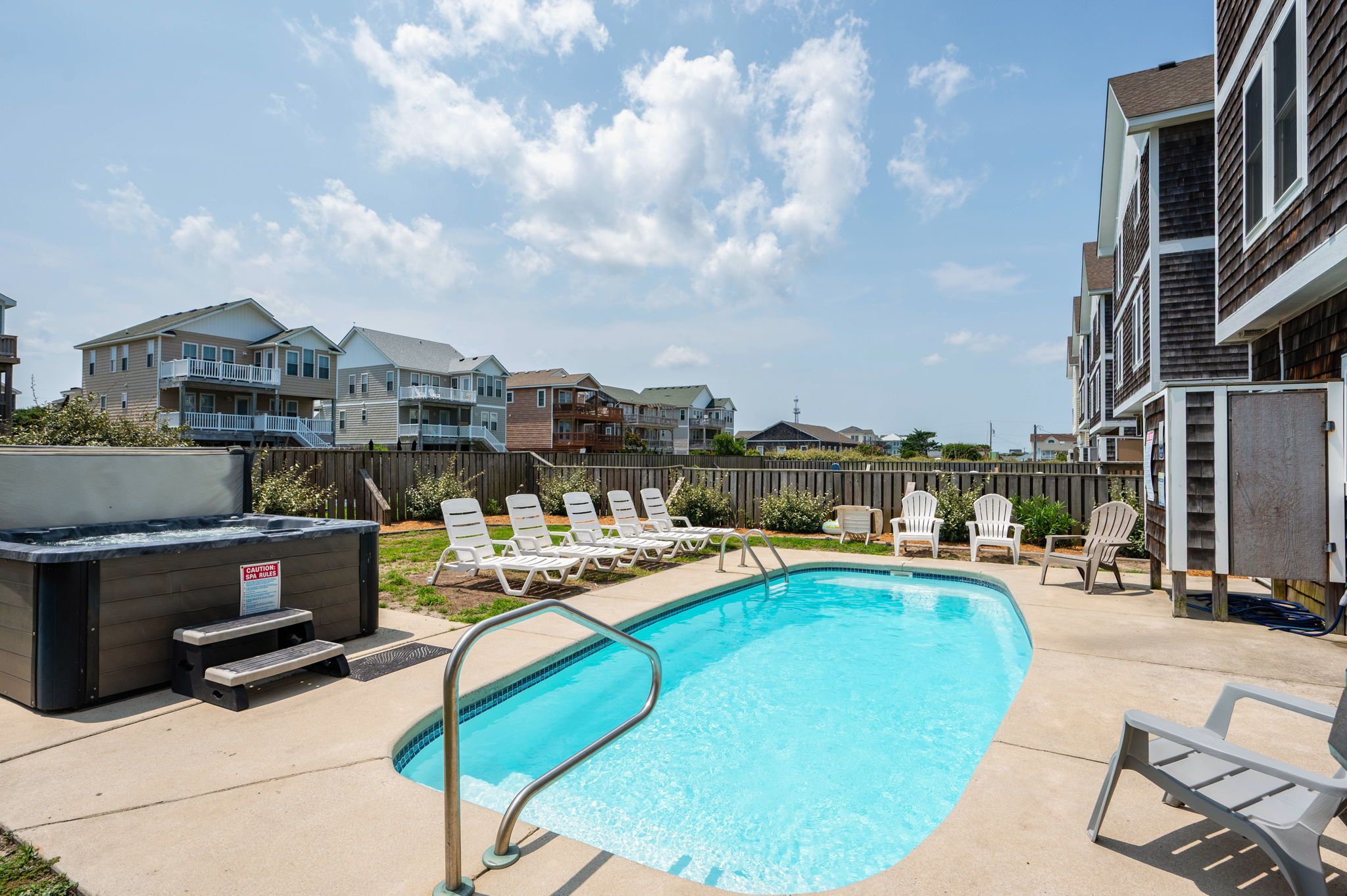 A swimming pool with lounge chairs, a hot tub, and a wooden fence.
