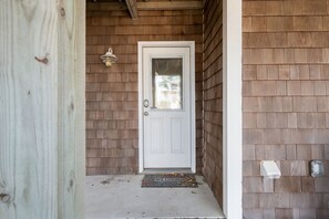 A wooden exterior with a white door, a doormat, and a small light fixture above the door.