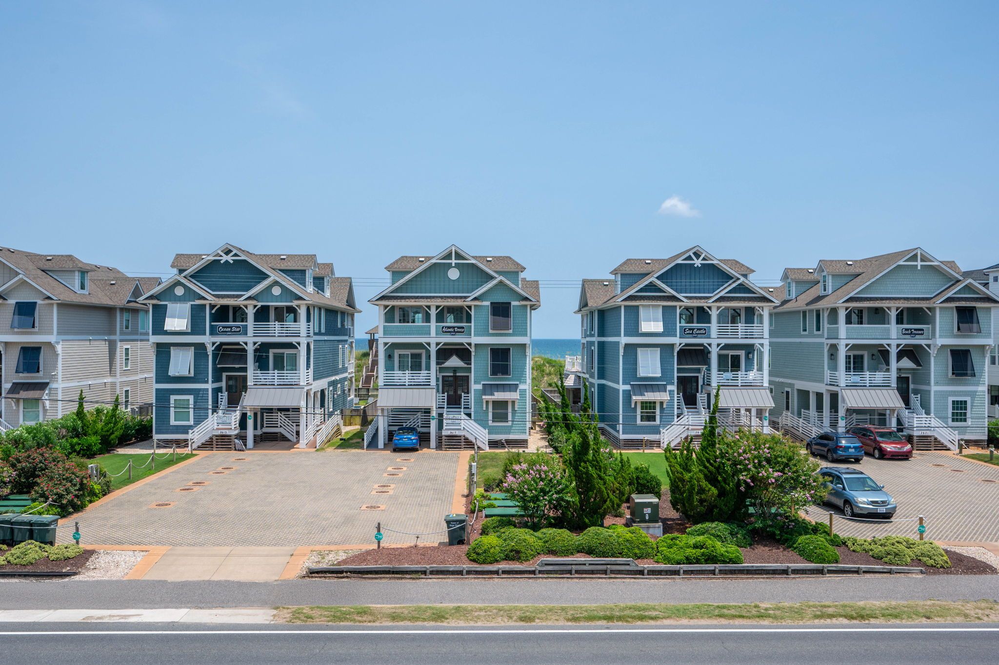 A row of beachfront condominiums with balconies, a parking area, and a clear view of the ocean.