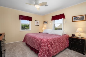 Quarto com cama, duas luminárias de cabeceira, ventilador de teto e janela com vista para o exterior.