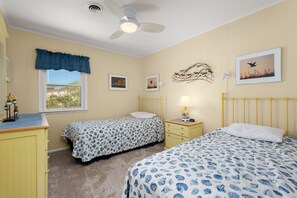 Un dormitorio con dos camas, una ventana, un ventilador de techo y decoración en la pared.